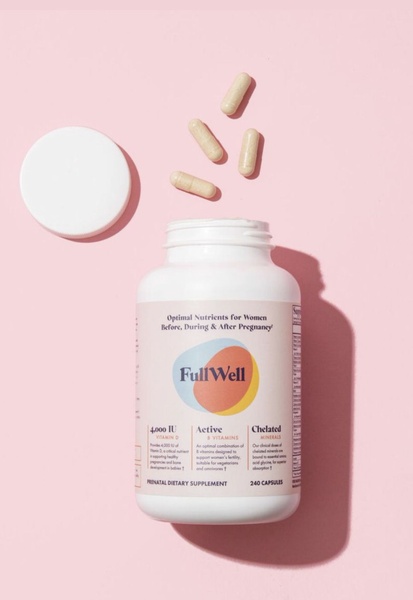 A high-quality product photography shot featuring a prenatal supplement bottle on a soft pink background with loose capsules for texture.
